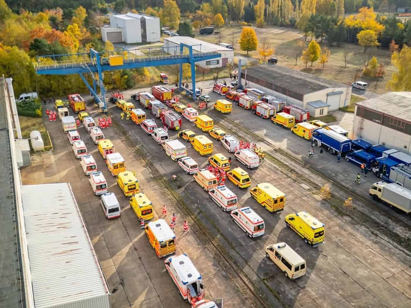 Luftaufnahme von Rettungswagen, Feuerwehrfahrzeugen und Einsatzkräften auf einem Übungsgelände
