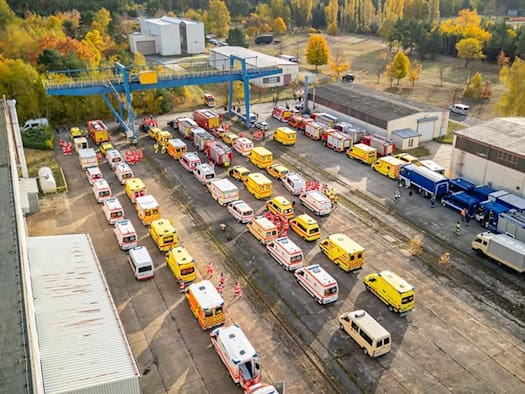 Luftaufnahme von Rettungswagen, Feuerwehrfahrzeugen und Einsatzkräften auf einem Übungsgelände