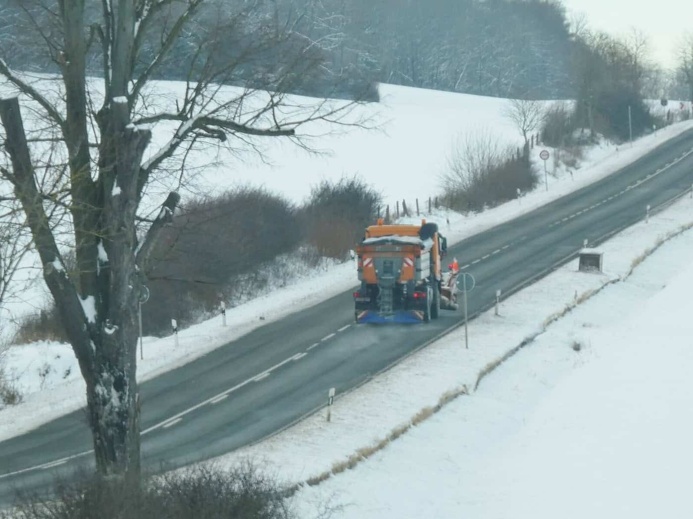Orangefarbenes Streufahrzeug auf einer verschneiten Landstraße