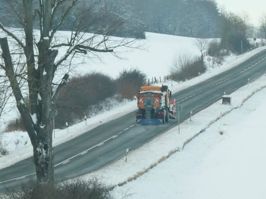 Orangefarbenes Streufahrzeug auf einer verschneiten Landstraße