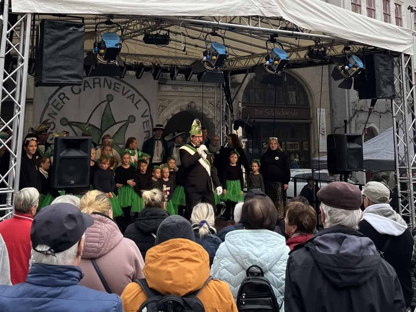 Karnevalisten und Kindergarde in Grün auf einer Bühne vor dem Meißner Rathaus, davor Publikum.