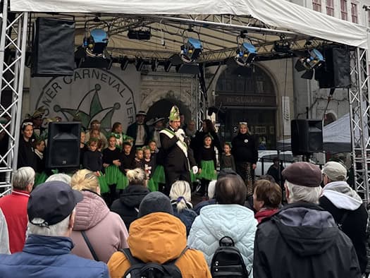 Karnevalisten und Kindergarde in Grün auf einer Bühne vor dem Meißner Rathaus, davor Publikum.