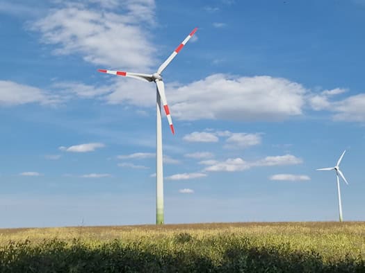 Zwei Windkraftanlagen auf einem Feld unter blauem Himmel