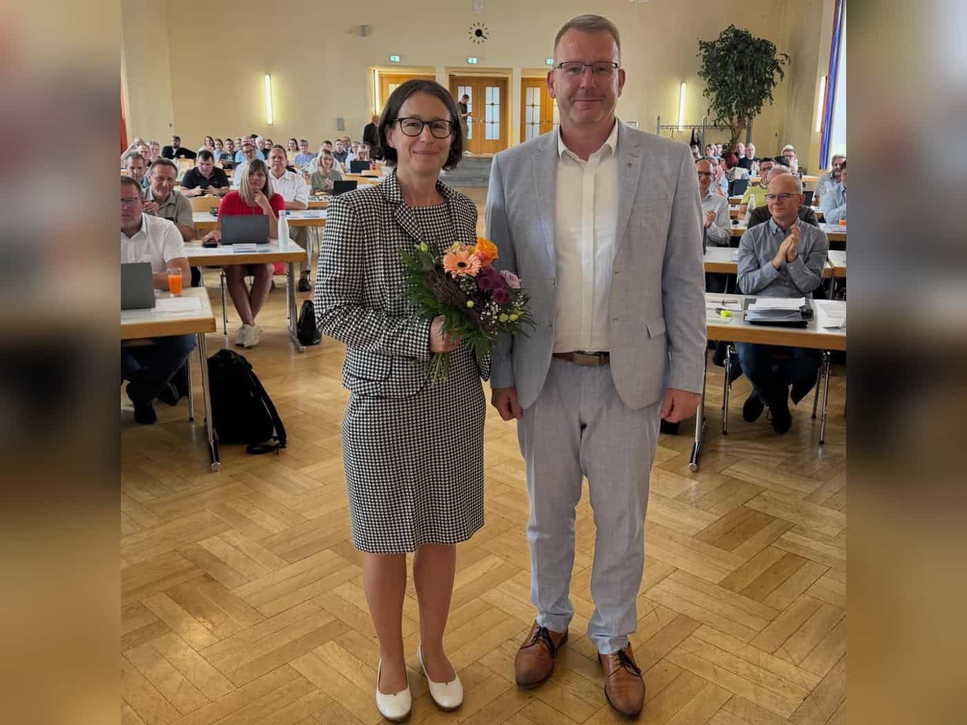 Pia Weißenberg mit Blumenstrauß neben Landrat Sven Krüger im Sitzungssaal des Kreistags