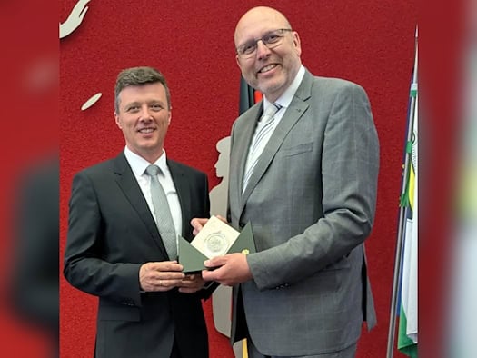 Markus Renner (links) und Olaf Raschke lächeln in die Kamera und halten gemeinsam eine aufgeklappte grüne Mappe mit einer Plakette.