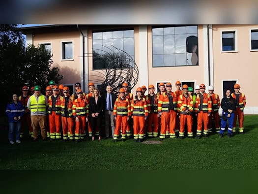 Gruppe von Auszubildenden und Studenten in orangefarbener Arbeitskleidung mit Schutzhelmen vor einem Gebäude in Italien
