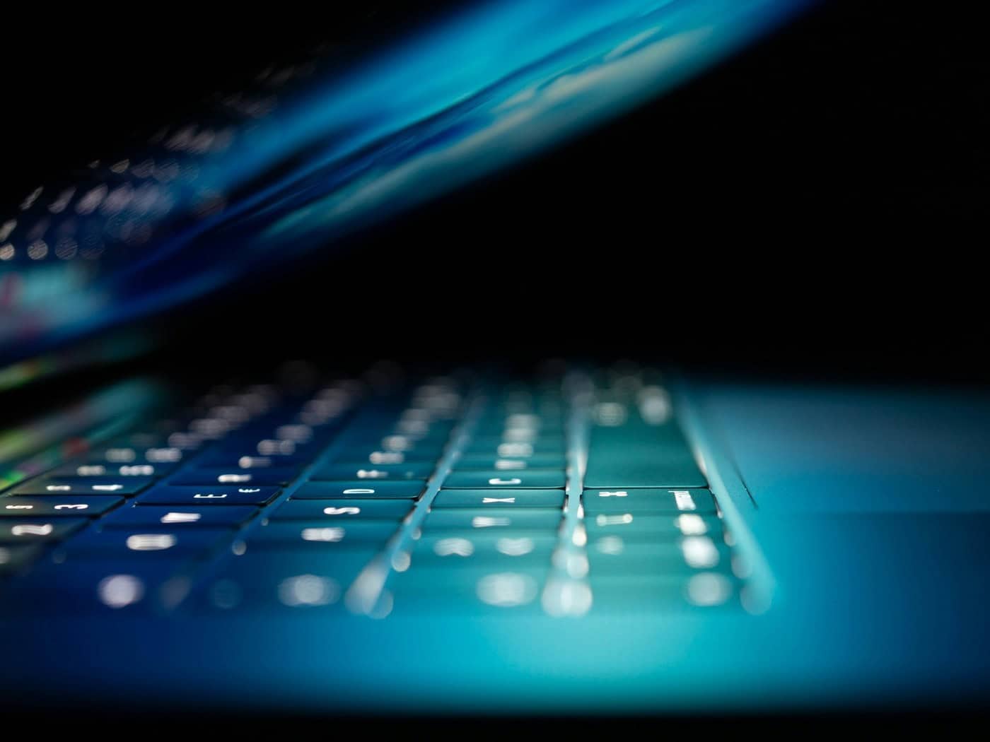 Beleuchtete Laptop-Tastatur in dunkler Umgebung, symbolisch für Betrug im Internet