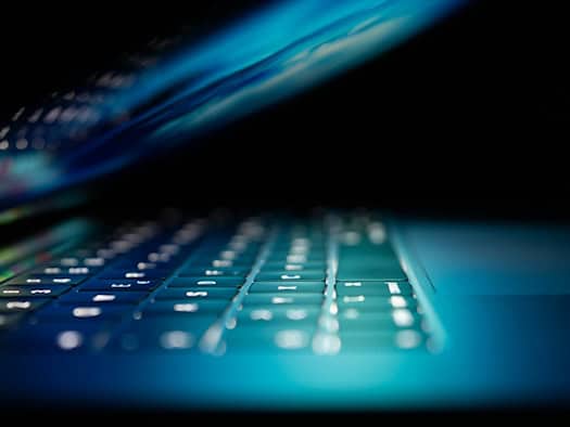Beleuchtete Laptop-Tastatur in dunkler Umgebung, symbolisch für Betrug im Internet