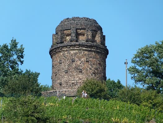 Der Bismarckturm in Radebeul aus Natursteinmauerwerk über einem Weinberg vor blauem Himmel