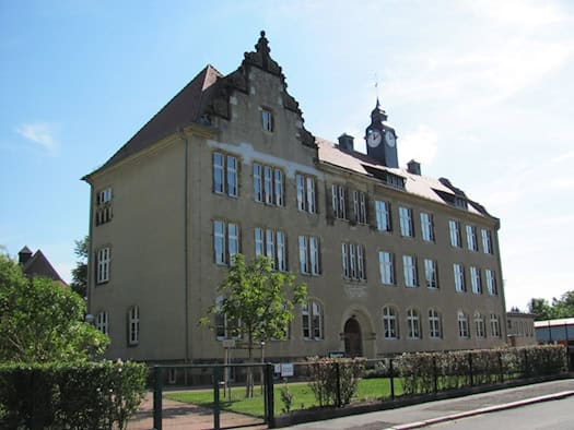 Dreistöckiges historisches Schulgebäude mit Uhrturm hinter einem grünen Zaun, Grundschule Naundorf in Radebeul