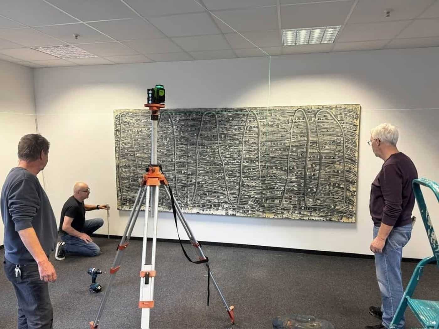 Drei Männer vor einem großformatigen abstrakten Gemälde beim Ausstellungsaufbau, einer kniet in der Mitte