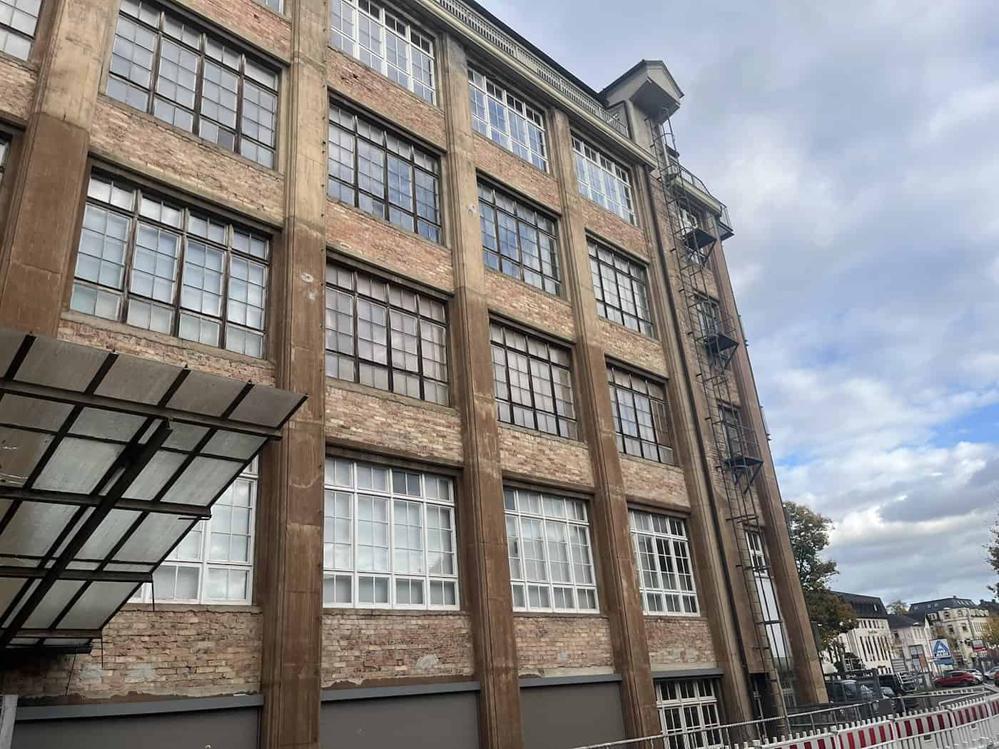 Steile Froschperspektive auf die vielgeschossige Backstein- und Klinkerfassade des Ernemann-Baus der Technischen Sammlungen Dresden mit vielen Sprossenfenstern. Rechts verläuft eine schmale metallene Fluchtleiter an der Außenwand nach oben.