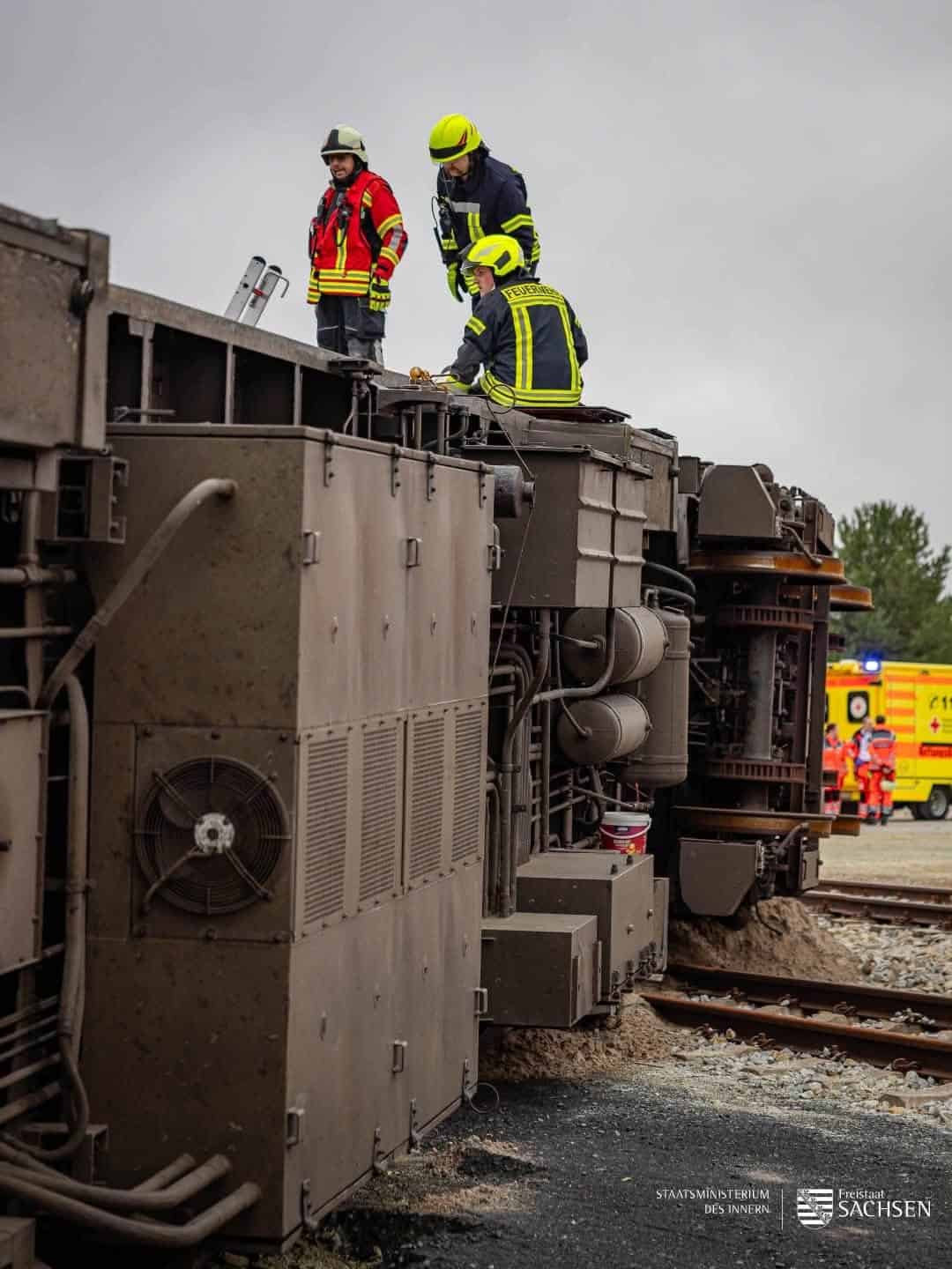 Feuerwehrleute stehen auf einem umgekippten Schienenfahrzeug bei der Übung MURE 26