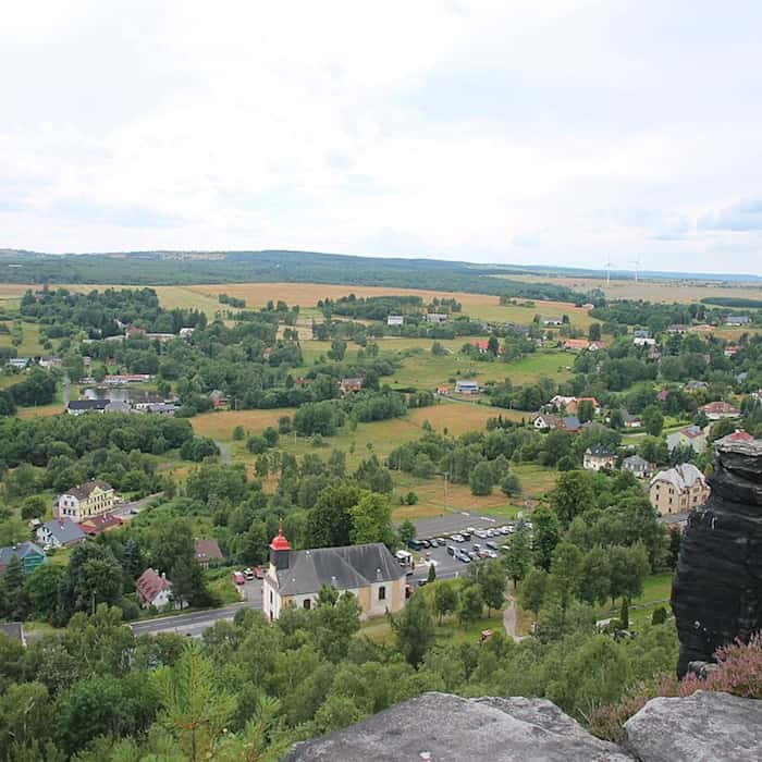 Blick von einem Sandsteinfelsen der Tyssaer Wände auf Tisá mit Kirche, Häusern und grüner Landschaft.