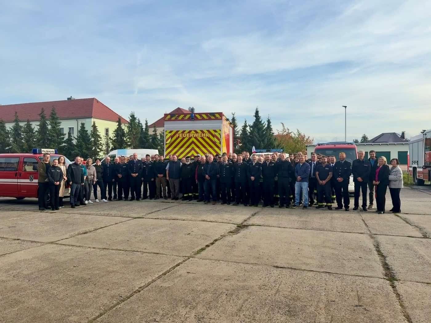 Feuerwehrleute und Gäste stehen vor Feuerwehrfahrzeugen auf einem Platz in Großenhain.