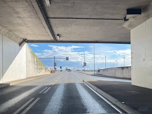 Blick aus der Windschutzscheibe eines Autos bei der Ausfahrt aus der hellgrauen Weströhre des Waldschlößchentunnels in Dresden auf die Fahrbahn in Richtung Waldschlösschenbrücke unter blauem, leicht bewölktem Himmel.