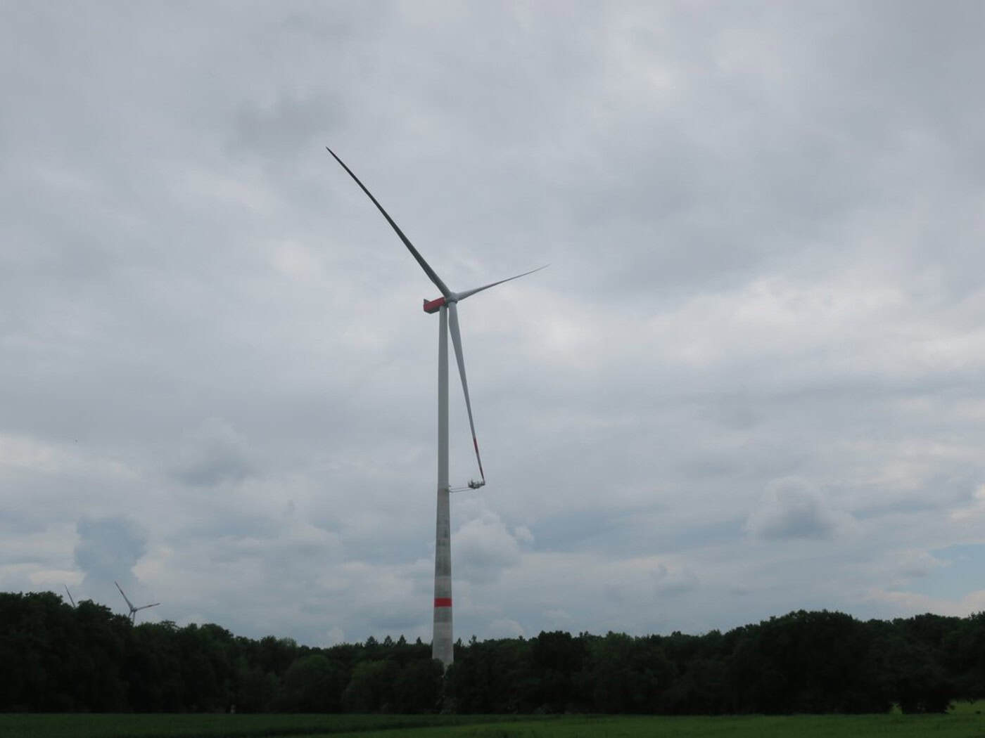 Weiße Windenergieanlage mit drei Rotorblättern auf einem Feld vor Himmel