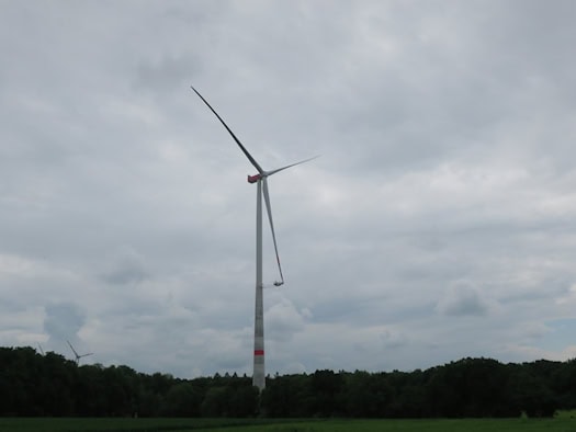Weiße Windenergieanlage mit drei Rotorblättern auf einem Feld vor Himmel