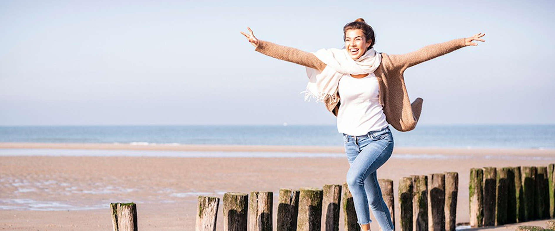 Junge Frau lacht glücklich am Meer, mit Sonne im Gesicht und Wind im Haar - ein Moment voller Lebensfreude.