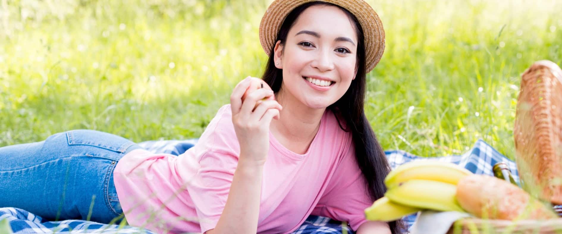 Frühling to go – Die besten Ideen für ein entspanntes Picknick Junge Frau liegt lächelnd auf einer Picknickdecke mit Picknickkorb – entspannter Frühlingsmoment unter freiem Himmel.