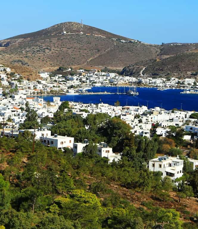 Blick über den Hafen von Patmos mit strahlend blauem Himmel, ruhigem Meer und sanften Hügeln im Hintergrund