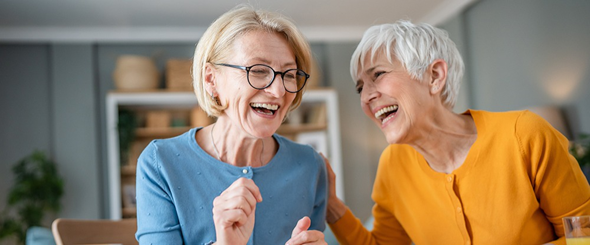 Zwei ältere Frauen lachen gemeinsam beim Spielen am Tisch, Symbolbild für Lebensfreude, soziale Verbundenheit und aktives Altern.
