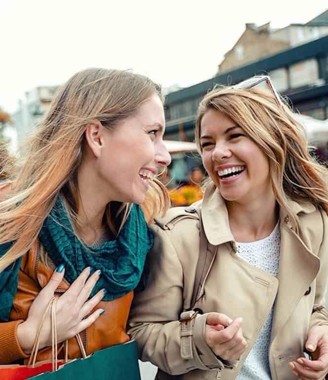 Zwei fröhliche Frauen beim Stadtbummel, lachen und genießen den Moment – Symbolbild für Lebensfreude, Wohlstand und alltägliches Glück.