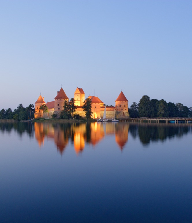 Die mittelalterliche Inselburg Trakai in Litauen, umgeben von Wasser und Wald, beleuchtet im warmen Licht eines Sommerabends.