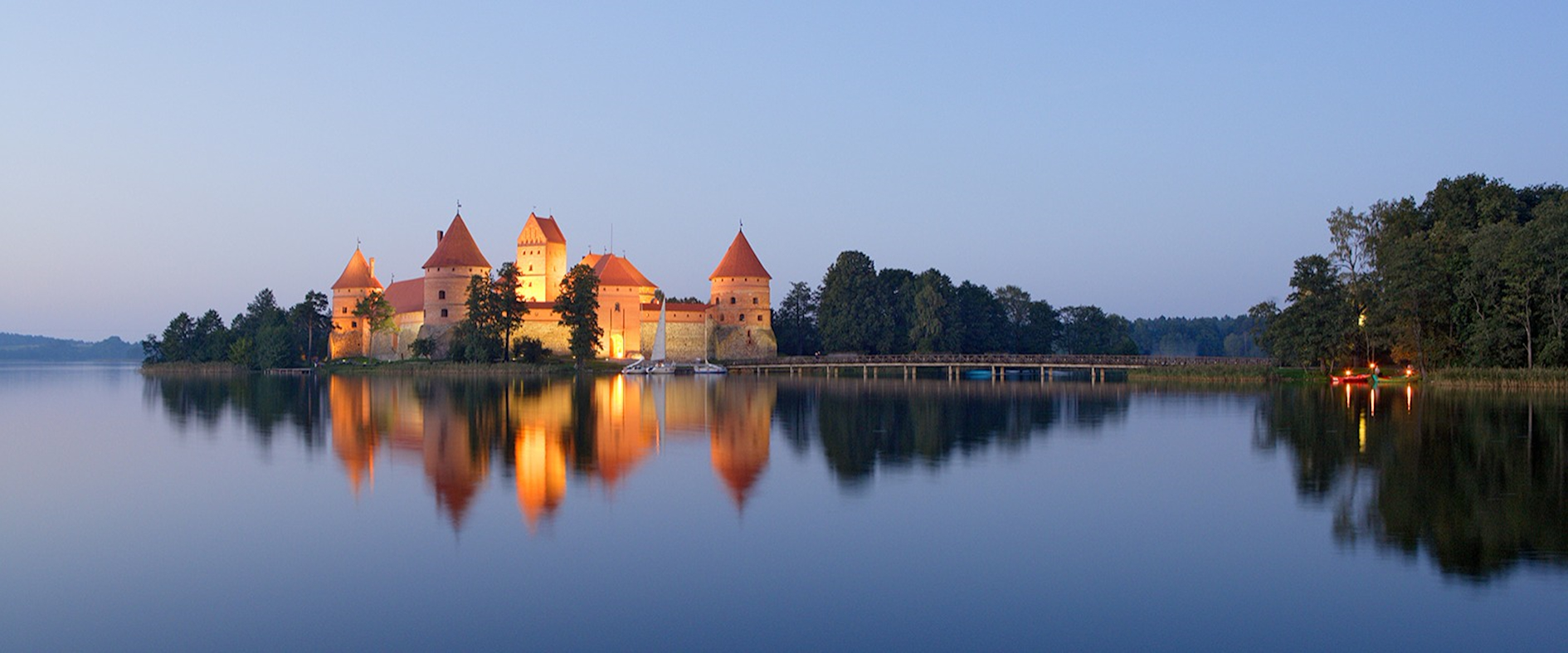 Die mittelalterliche Inselburg Trakai in Litauen, umgeben von Wasser und Wald, beleuchtet im warmen Licht eines Sommerabends.