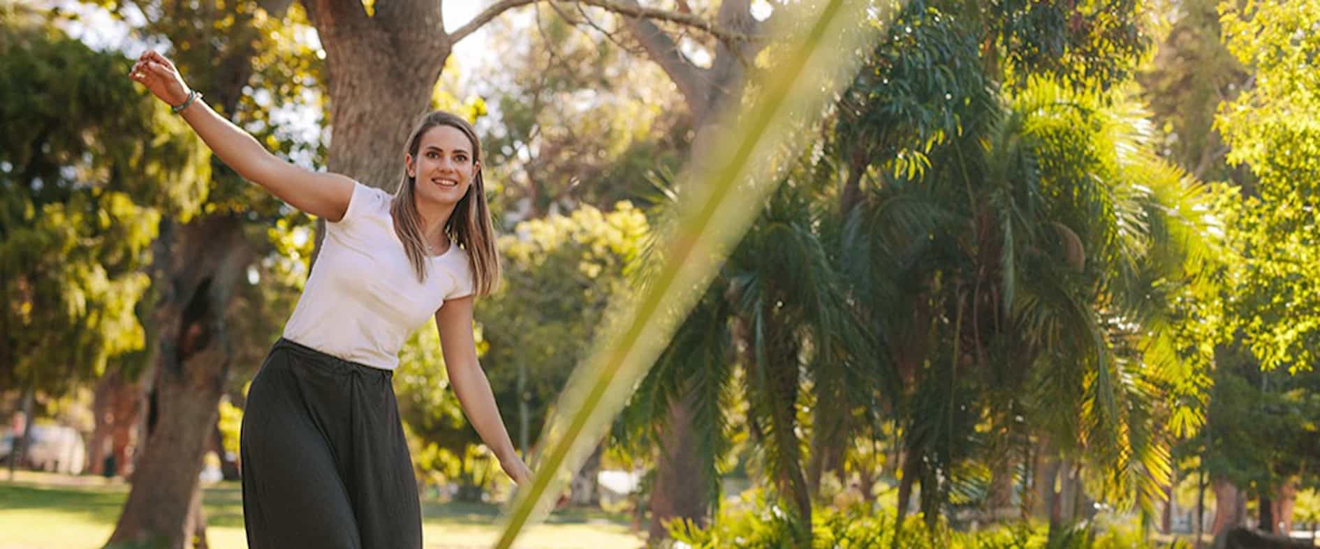 Junge Frau balanciert auf einer Slackline in einem sonnigen Park – Symbol für innere Balance und aktives Glückstraining.