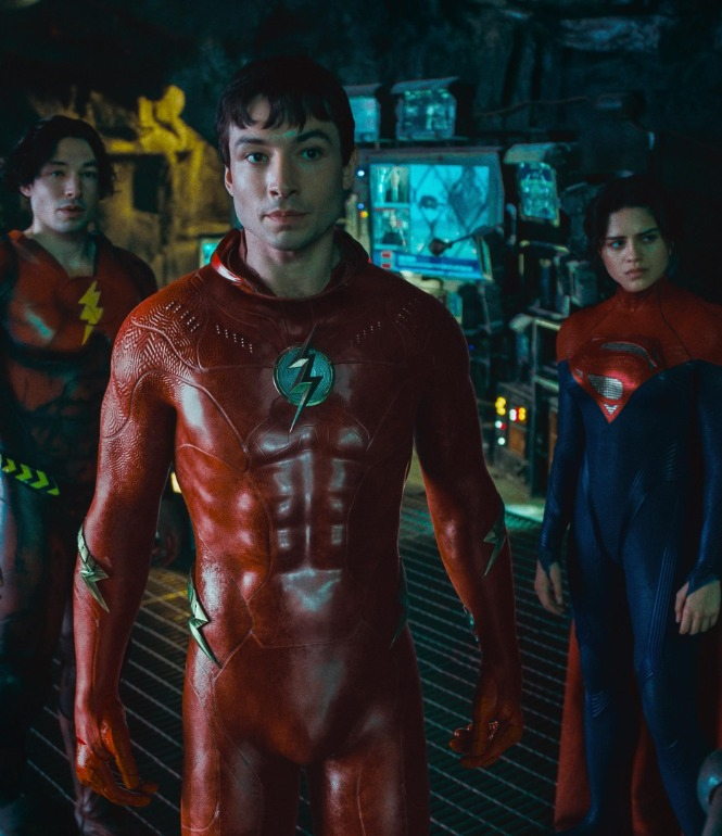 Drei Superhelden in einer dunklen Hightech-Umgebung: Zwei Versionen von The Flash und Supergirl blicken entschlossen nach vorn – Szene aus dem Film „The Flash“.