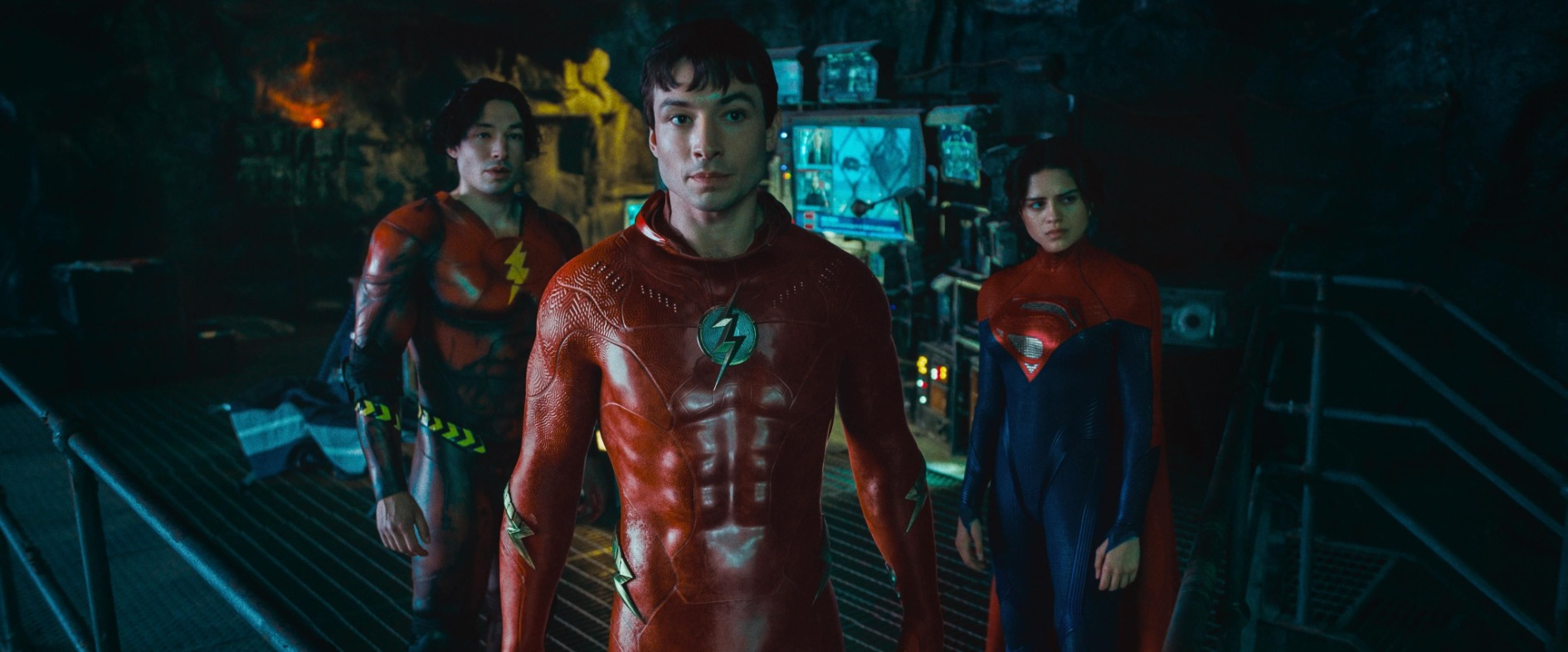 Drei Superhelden in einer dunklen Hightech-Umgebung: Zwei Versionen von The Flash und Supergirl blicken entschlossen nach vorn – Szene aus dem Film „The Flash“.