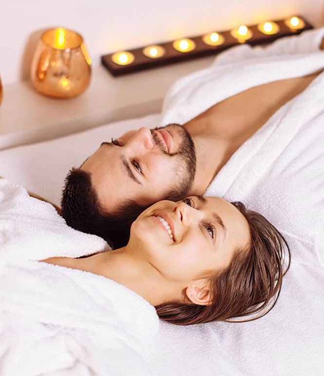 Paar in weißen Bademänteln entspannt gemeinsam im Spa bei Kerzenschein