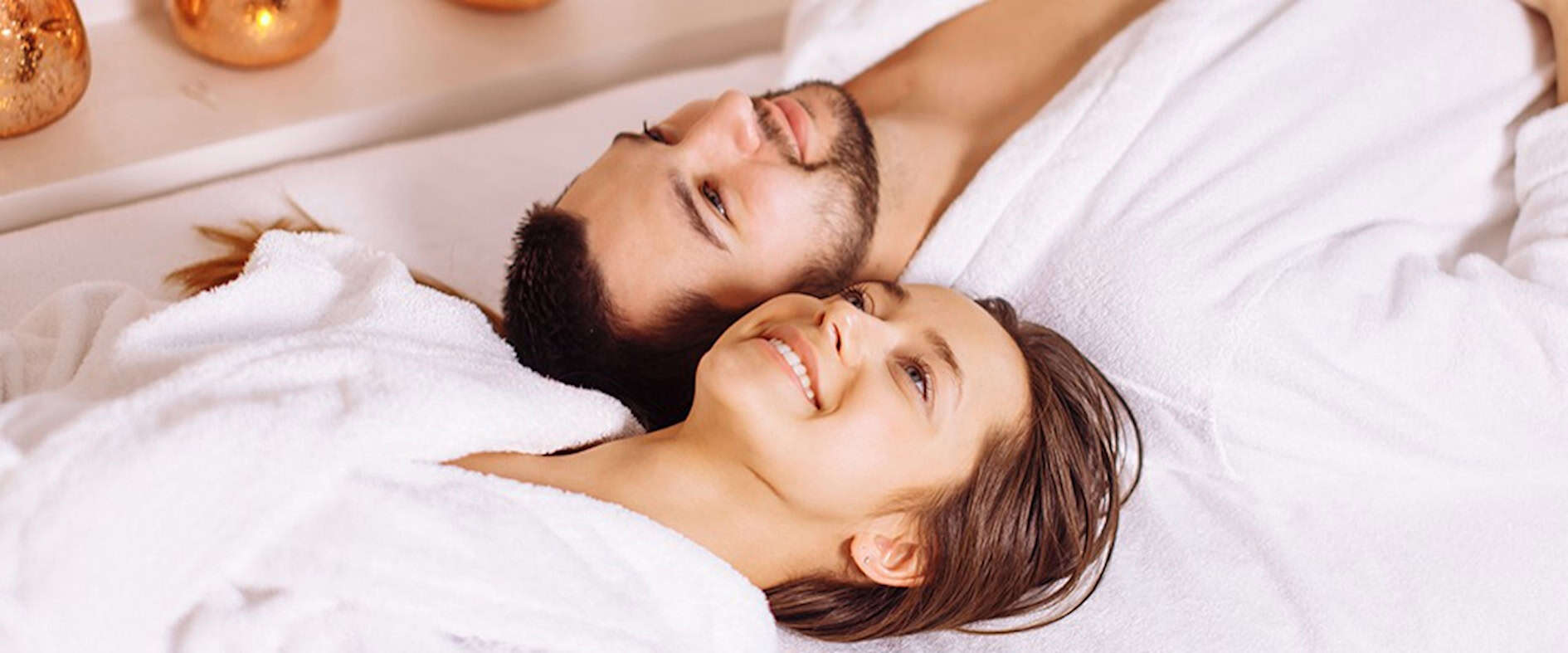 Paar in weißen Bademänteln entspannt gemeinsam im Spa bei Kerzenschein