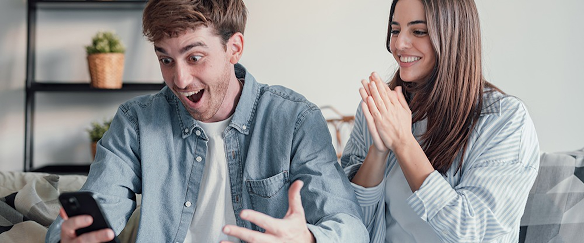 Mann und Frau freuen sich gemeinsam auf dem Sofa über eine Nachricht auf dem Smartphone, symbolisch für einen doppelten Lottogewinn.