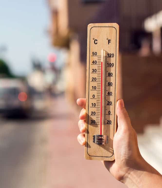 Hand hält Thermometer mit über 40 Grad Celsius auf heißer Stadtstraße