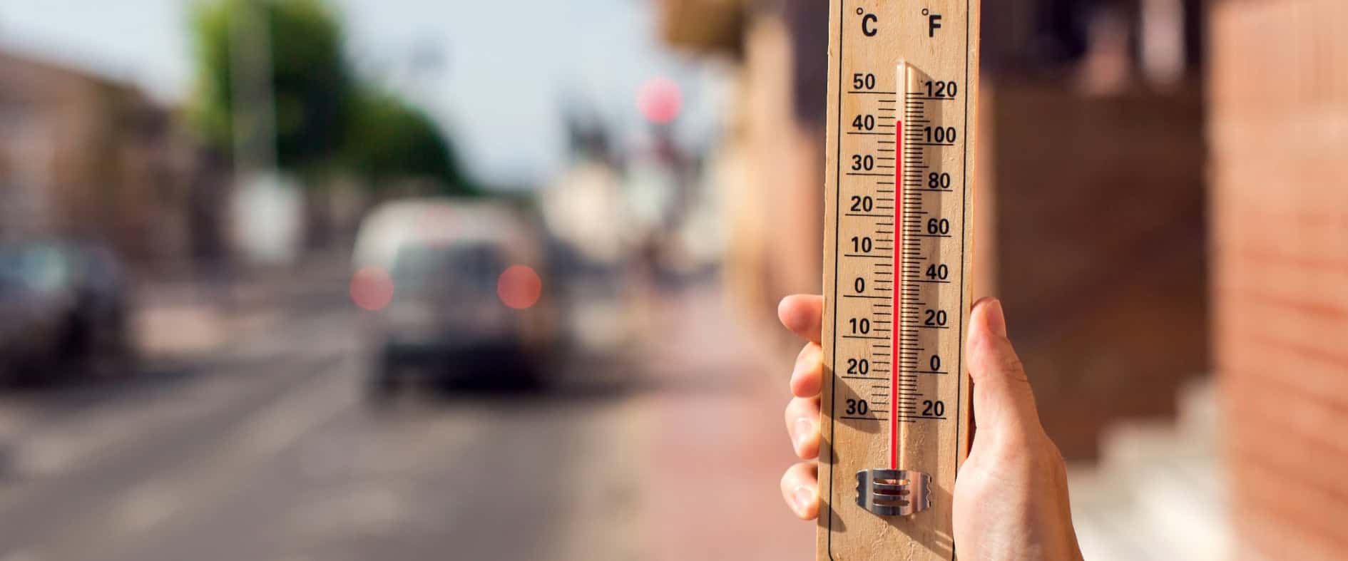 Hand hält Thermometer mit über 40 Grad Celsius auf heißer Stadtstraße