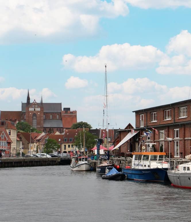 Alter Hafen von Wismar mit Blick auf historische Backsteingebäude und die St.-Georgen-Kirche im Hintergrund.