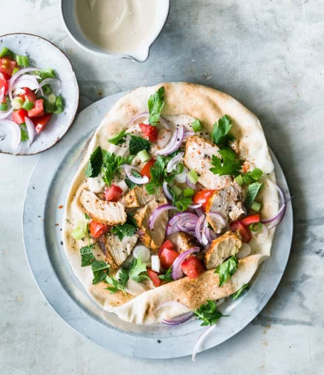 Fladenbrot mit gegrilltem Shawarma-Hähnchen, Tomaten, roten Zwiebeln, Frühlingszwiebeln, frischen Kräutern und Tahina-Dip, angerichtet auf einem Teller.