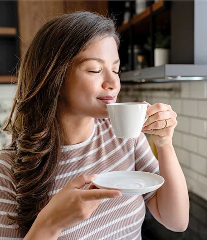 Junge Frau trinkt genussvoll eine Tasse Kaffee und erlebt den Glücksmoment am Morgen.
