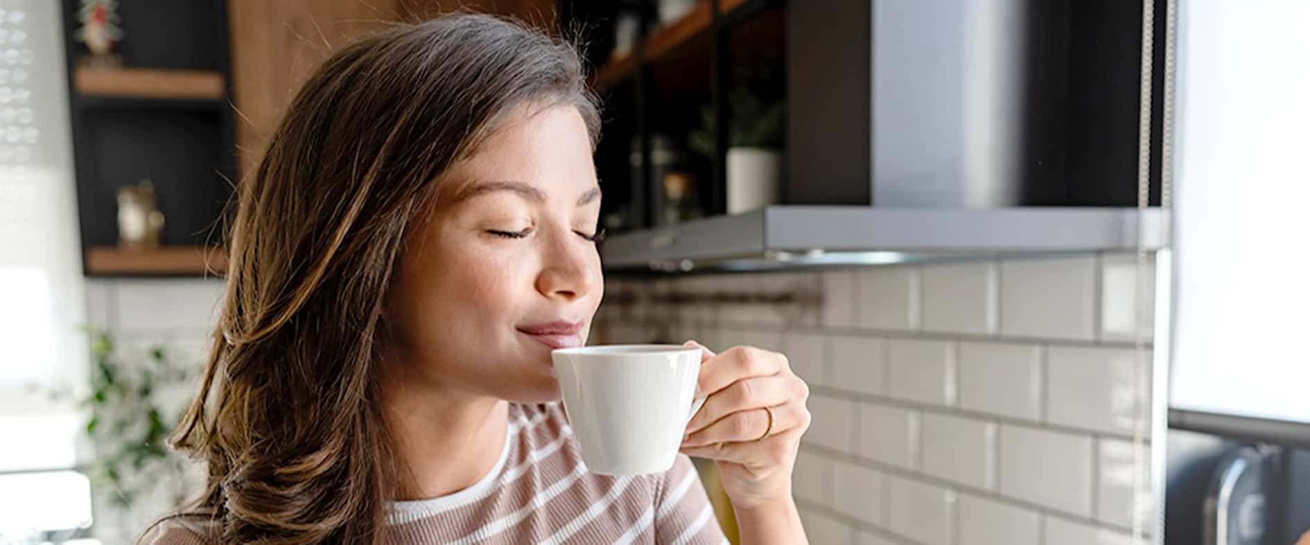 Junge Frau trinkt genussvoll eine Tasse Kaffee und erlebt den Glücksmoment am Morgen.