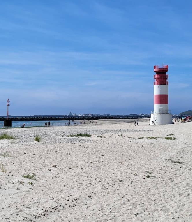 Blick auf einen Sandstrand mit Leuchtturm auf der Helgoländer Düne, im Hintergrund blauer Himmel und ruhiges Meer – typisch für den Südstrand der Insel.