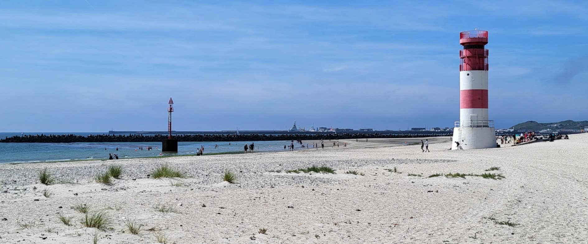 Blick auf einen Sandstrand mit Leuchtturm auf der Helgoländer Düne, im Hintergrund blauer Himmel und ruhiges Meer – typisch für den Südstrand der Insel.
