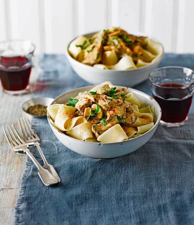 Schüsseln mit cremigem Rinder-Stroganoff und Pappardelle, garniert mit frischer Petersilie, serviert auf einem gedeckten Tisch.