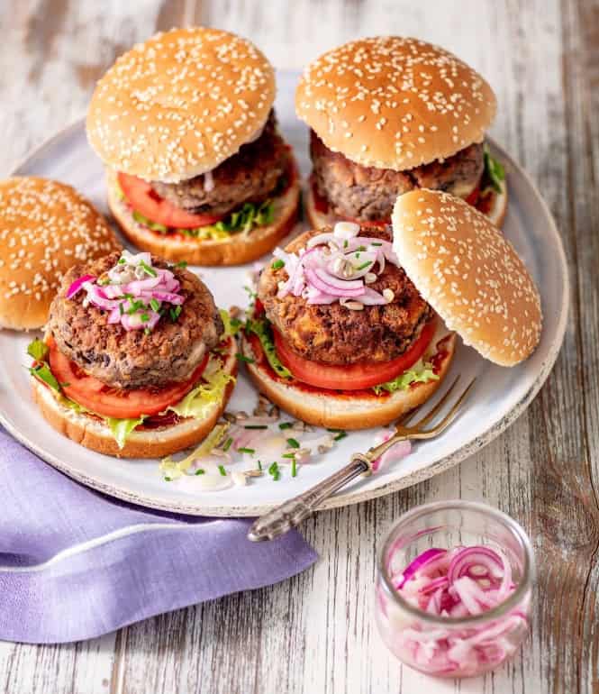 Vegetarische Kidneybohnenburger mit Tomaten, Salat, eingelegten roten Zwiebeln und Sesambrötchen, angerichtet auf einem Teller.