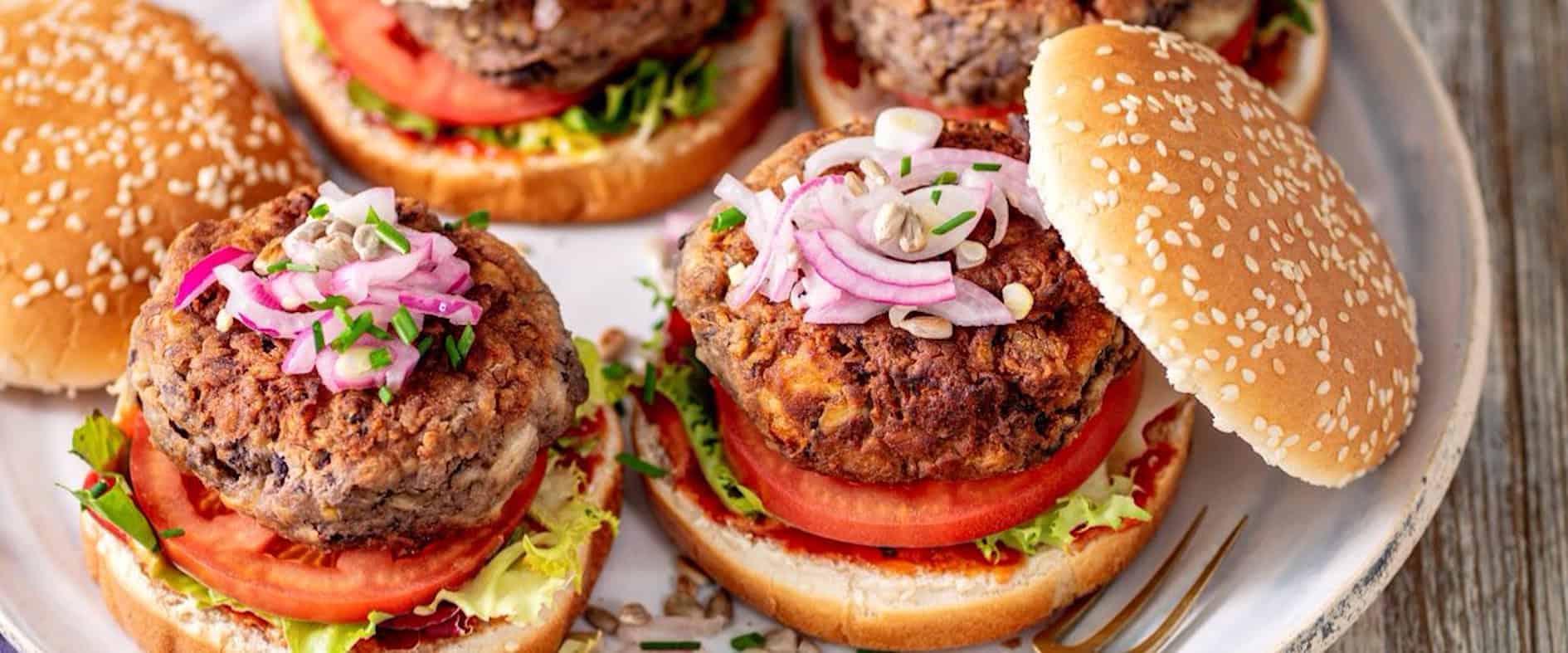 Vegetarische Kidneybohnenburger mit Tomaten, Salat, eingelegten roten Zwiebeln und Sesambrötchen, angerichtet auf einem Teller.