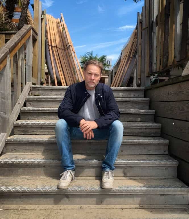 Janek Rieke sitzt auf einer Holztreppe und spricht im Interview über seinen Kinofilm  „Beule – Zerlegt die Welt“.
