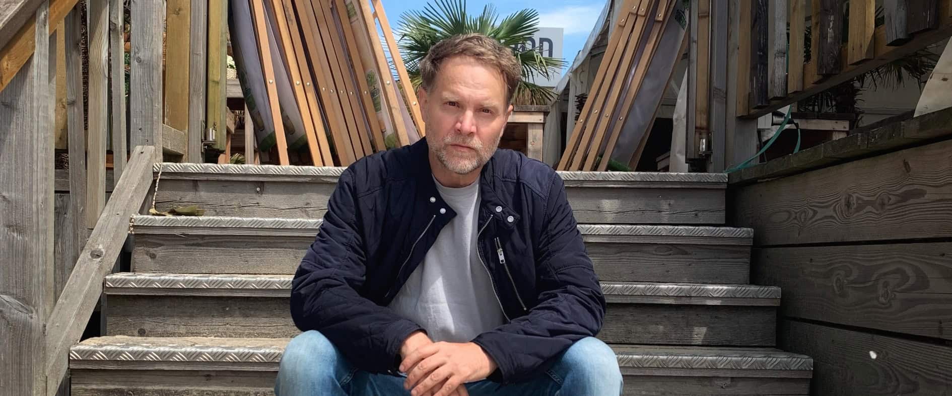 Janek Rieke sitzt auf einer Holztreppe und spricht im Interview über seinen Kinofilm  „Beule – Zerlegt die Welt“.
