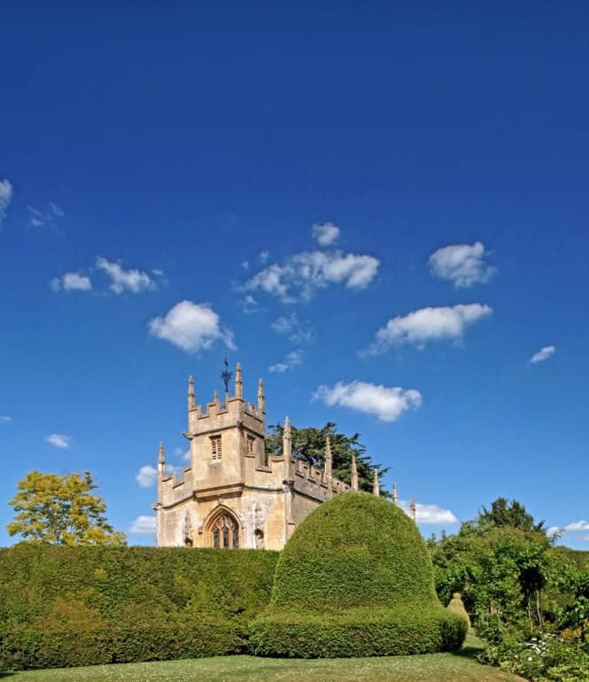 Schlosskapelle von Sudeley Castle in Cheltenham, umgeben von Gärten und Hecken unter blauem Himmel in den Cotswolds.