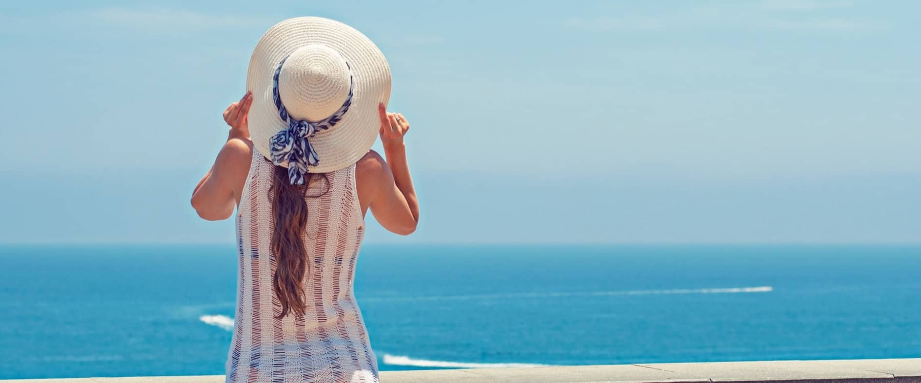 Frau mit Sonnenhut blickt aufs Meer und genießt den Moment der Ruhe